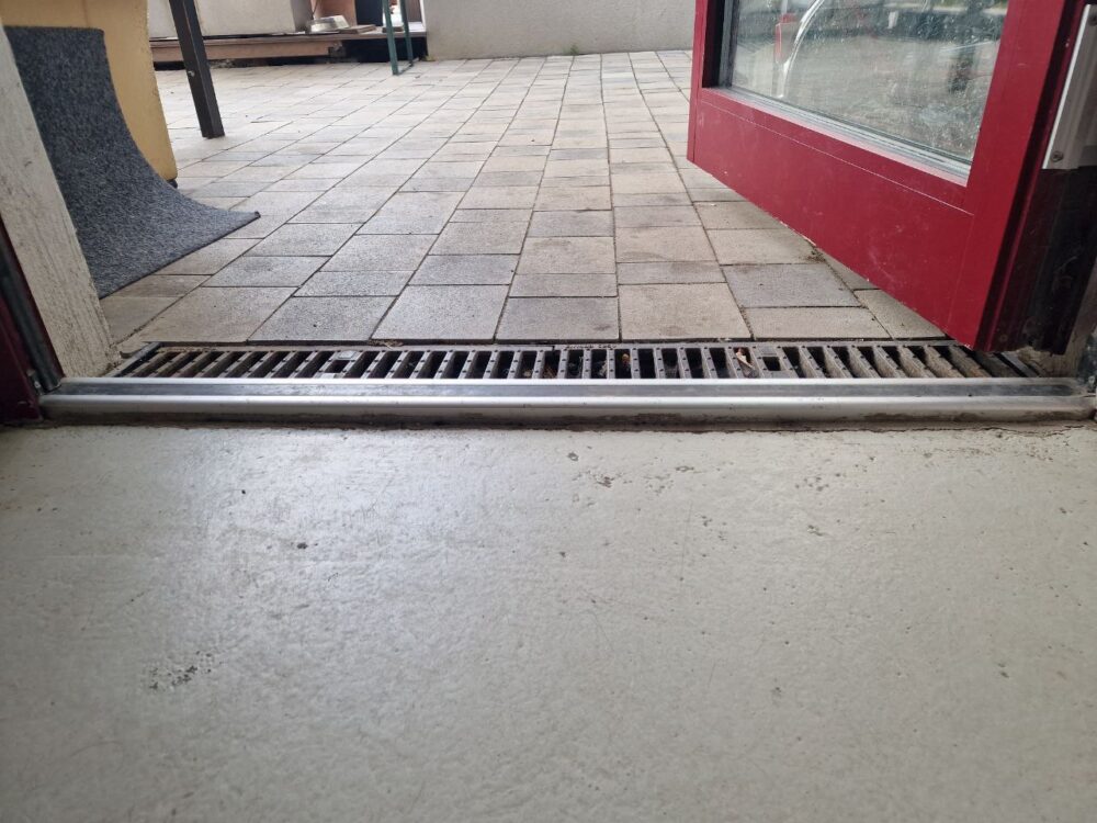 Türschwelle mit leichter Erhöhung zwischen Innenraum und gepflastertem Außenbereich.